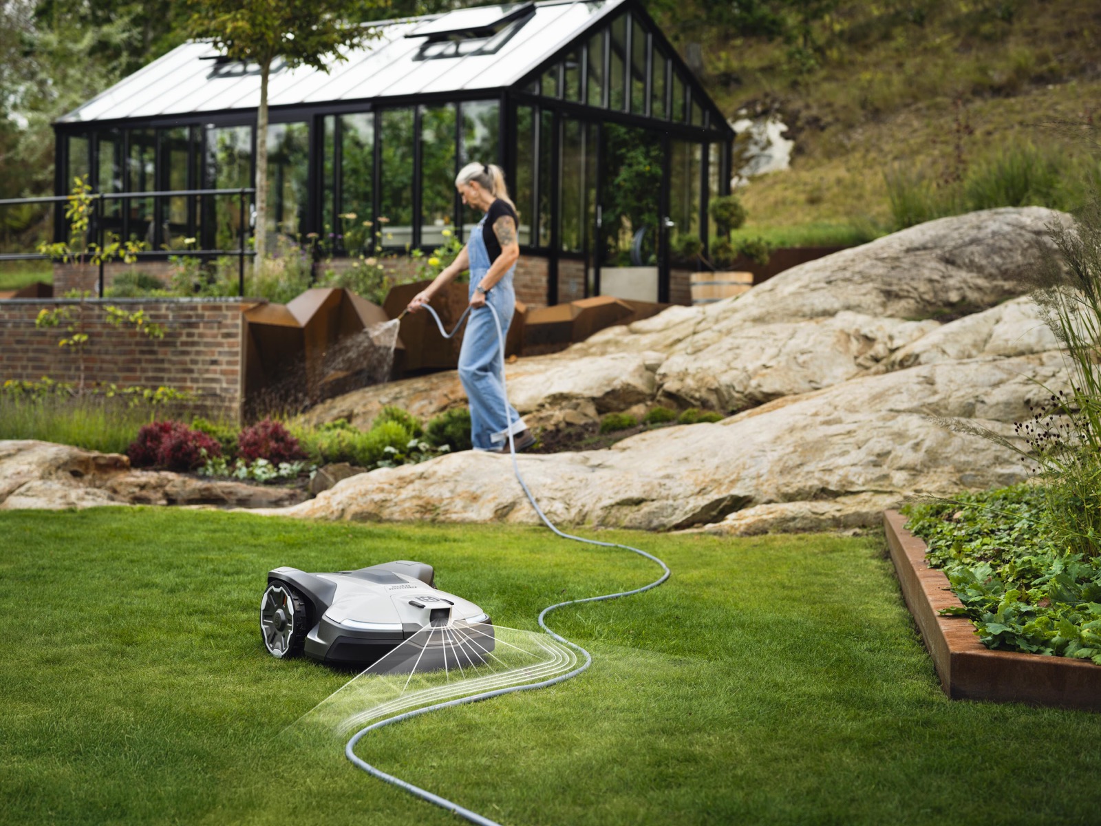 Husqvarna Automower NERA klipper en solrik hage med drivhus i bakgrunnen
