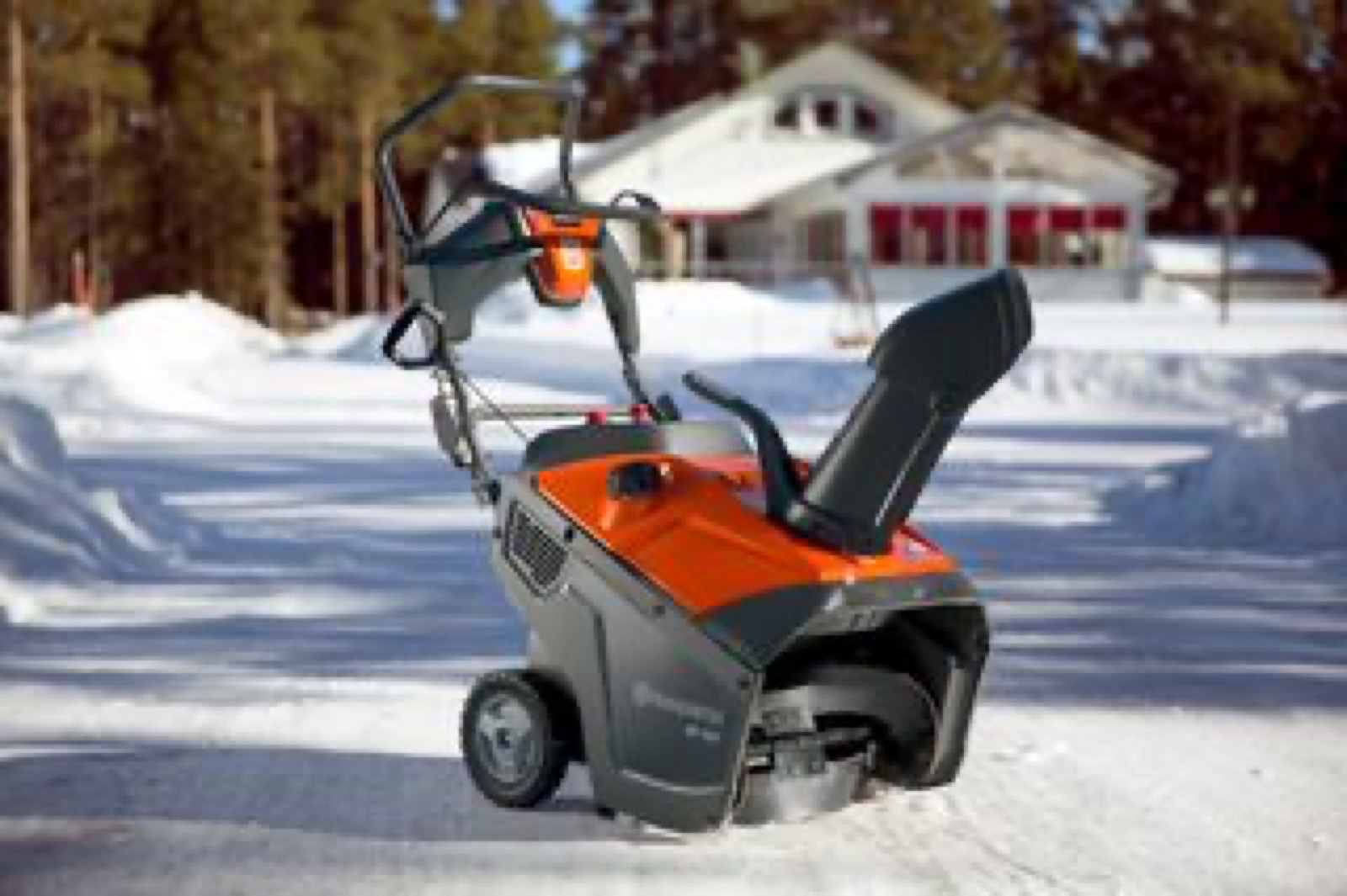Husqvarna ettrinns snøfreser på en brøytet oppkjørsel foran et hus i sol og blå himmel